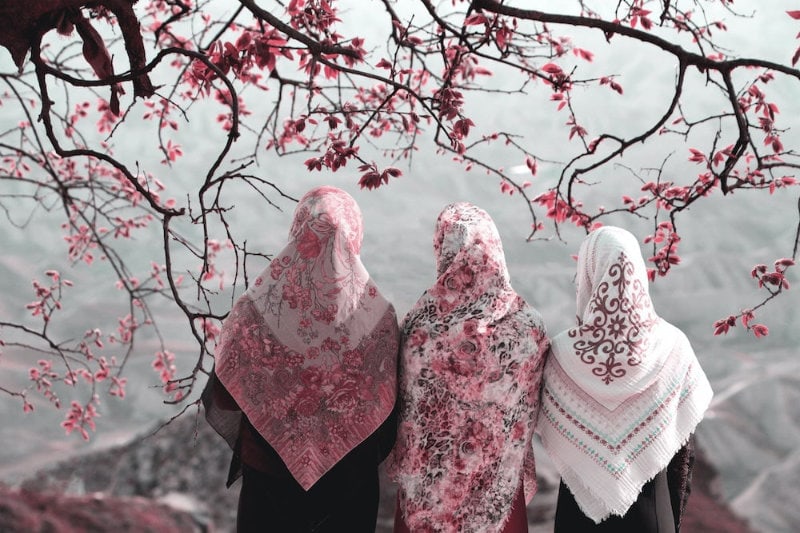 Three women in pink floral hijabs surrounded by flowering tree